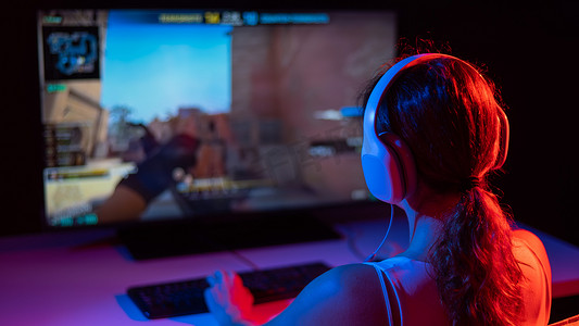 游戏大全摄影照片_一名白人妇女在黑暗中的霓虹灯下玩电脑游戏的后视图。