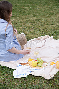 一位身穿蓝色连衣裙、头戴草帽的年轻女子正在野餐时休息，上面有水果