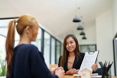 一位亚洲女银行员工的画像，要求客户在签署前阅读合同以同意购买房屋、房地产概念