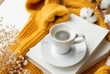 暖黄色毛衣、白书、一杯热咖啡和干花的舒适组合，顶视图