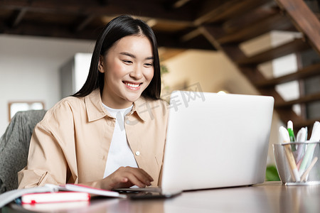 微笑的亚洲女孩观看网络研讨会，在家进行工作视频通话，远程自由职业，看着电脑很开心