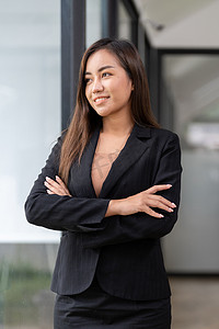 穿着黑色西装、微笑、交叉双手自信地望着外面的亚洲职业女性画像