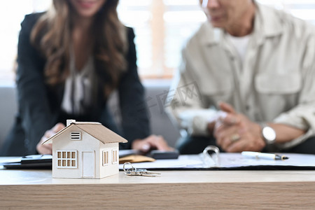 木桌上的小房子模型与老人在后台与财务顾问讨论购房问题。