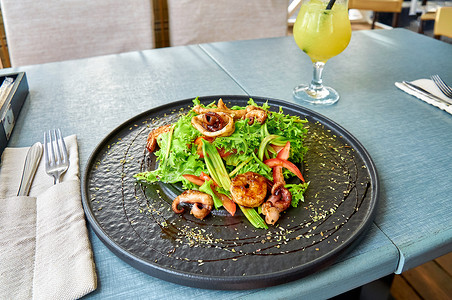 餐厅阳台上的黑盘上放着新鲜的地中海沙拉，配有虾、章鱼和鱿鱼