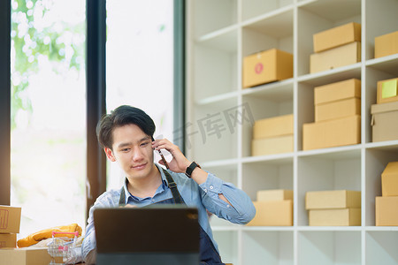 一家小型初创企业和中小企业主的肖像，一位亚洲男性企业家使用手机检查订单以整理产品，然后将它们包装到客户的内盒中