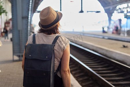 戴帽子、背包的成熟女性在火车站站台上行走