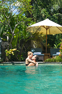 幸福的情侣在巴厘岛乌布郁郁葱葱的热带植物环绕的室外水疗无边泳池中放松时亲吻。