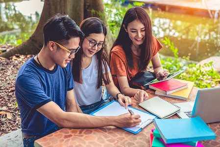 咱做朋友吧摄影照片_一群亚洲大学生在户外的桌子上读书并辅导特殊课程的考试。