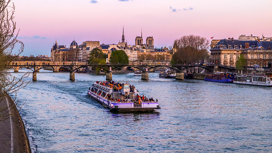 游船、横跨塞纳河的最古老的桥梁 (Pont Neuf) 和日落时法国巴黎的历史建筑。 