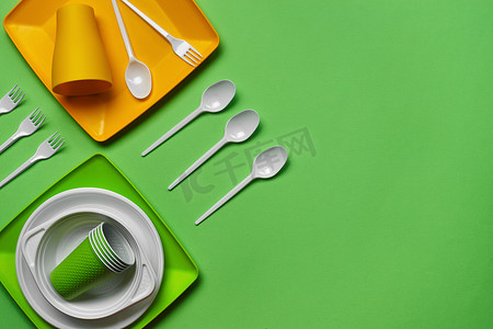 在绿色背景的五颜六色的塑料一次性餐具与拷贝空间。