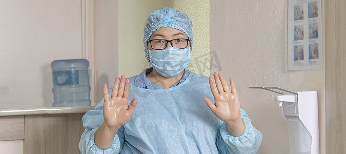 消毒液手摄影照片_横幅上有身穿一次性医疗服、头戴医用帽和戴眼镜的医务人员的横幅，上面显示了经过治疗的手，肘部分配器旁边有消毒液。