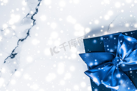 节日礼盒摄影照片_冬季节日礼盒，配有蓝色丝绸蝴蝶结、大理石背景上的雪花，作为豪华美容品牌的圣诞和新年礼物，平铺设计