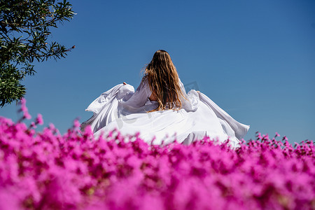 一位身穿白色飘逸长裙的美女，靠近一片后视粉色花朵的美丽田野