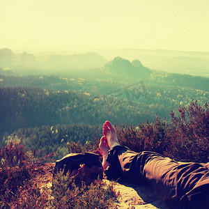 穿着深色远足裤的疲惫的长腿在山谷上方的岩石峰上休息。