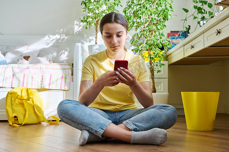 使用智能手机的少女坐在家里房间的地板上休息