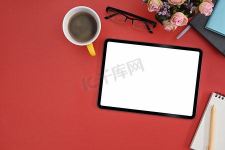 平躺式数字平板电脑，配有空显示屏、咖啡杯、笔记本和红色背景的眼镜。