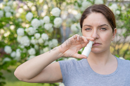 鼻腔喷雾剂摄影照片_白人妇女在公园散步时使用鼻喷雾剂。
