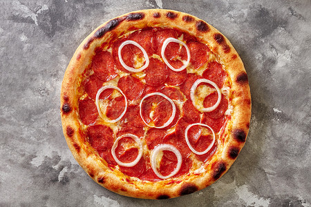 灰色石头上的意大利辣香肠披萨配番茄酱、马苏里拉奶酪和洋葱圈的顶部景色