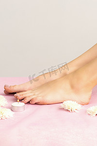 粉红色沙发上点着蜡烛和鲜花的年轻女子美丽的白色光滑脚。