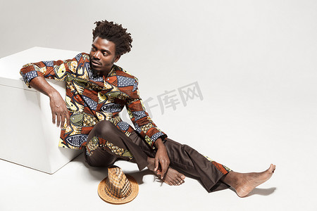 想知道穿着传统服装的非洲男人坐在立方体上。