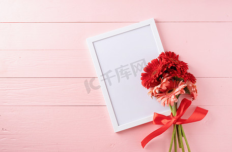 粉色木桌上的红色非洲菊雏菊花和空白白框