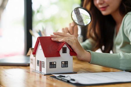 一名妇女拿着放大镜检查房屋模型。房地产房屋评估和检查概念。