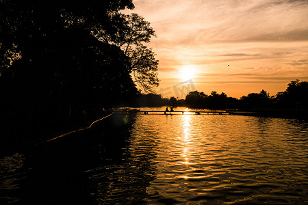 橙色浪漫摄影照片_日落时的湖景与情侣在湖橙色日落时的背光剪影。