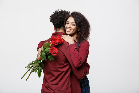 情侣概念-年轻的非洲裔美国夫妇互相拥抱，手捧浪漫的红玫瑰。