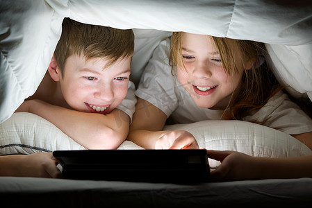 玩电脑看手机摄影照片_孩子们晚上盖着毯子在平板电脑上玩游戏，孩子们在平板电脑上看视频。