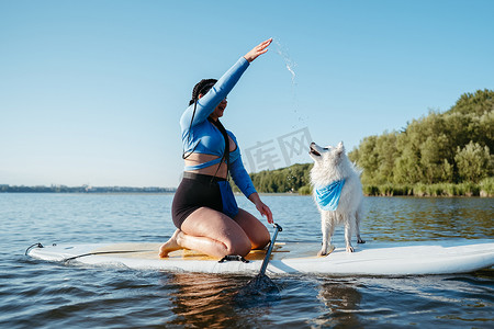 带着 Locs 的女人坐在湖边的冲浪板上和她的宠物日本狐狸玩耍