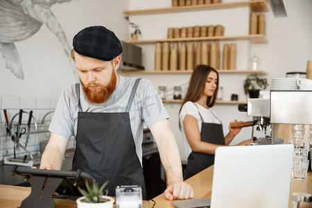 咖啡业务概念-年轻英俊的大胡子调酒师、咖啡师或经理在现代咖啡店的数字平板电脑菜单中发布客人的订单。