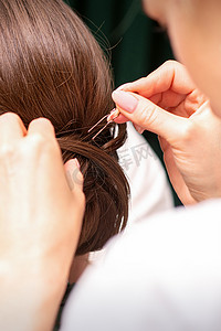做发型摄影照片_一位美发师正在美发沙龙里为一位年轻的黑发女子做发型，特写。