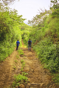 男人走路摄影照片_两个男人在穿过乡村的小路上，两个年轻人沿着有复制空间的小路行走