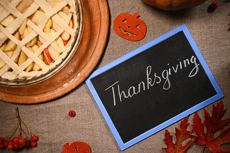 黑板上写着感恩节的字样，桌布上有苹果和片状外壳的南瓜派的部分景色