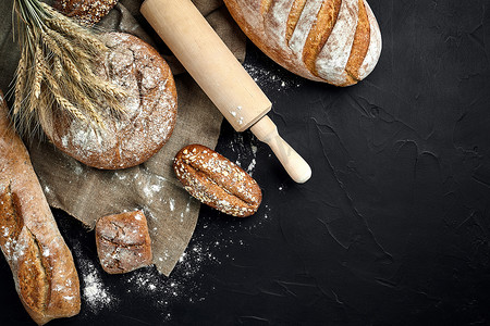 撒面粉摄影照片_法式长棍面包、烤面包、面粉和小麦穗组合物的顶视图，深色背景上撒有小麦粉