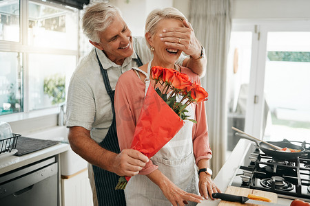 生日会摄影照片_当男人在周年纪念日、生日或情人节那天在厨房里送给妻子一束玫瑰花时，年长夫妇会遮住眼睛和鲜花。