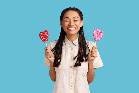 齿形边框摄影照片_女人拿着甜蜜的心形糖果棒棒糖，带着露齿的微笑看着相机。