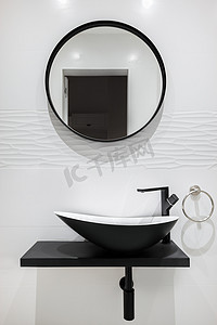带黑色水龙头和盆和圆镜的白色瓷砖浴室。