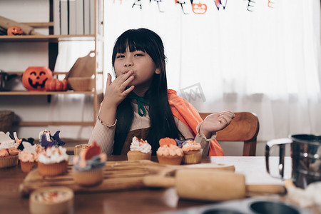 万圣节的小女孩在桌子上制作零食和纸杯蛋糕。