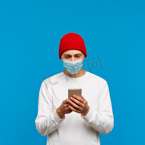 手机病毒摄影照片_戴着医疗防护面罩、用手机发短信的男子肖像。