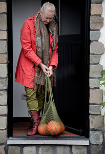 国家网摄影照片_一位穿着红色斗篷、带着橙色南瓜网的中年妇女打开了门