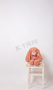 粉红色的兔子毛绒娃娃坐在白色背景的凳子上。