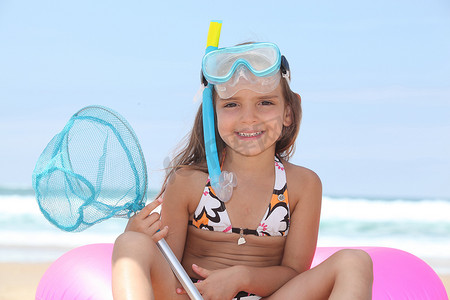 海滩上带通气管、面具和渔网的小女孩
