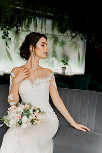 穿着婚纱和新娘面纱的新娘坐在咖啡馆的时尚椅子上。