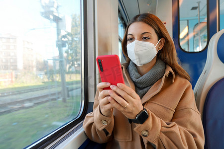 医学通摄影照片_戴着面罩 FFP2 KN95 的年轻女性在乘坐公共交通工具的智能手机上阅读冠状病毒。