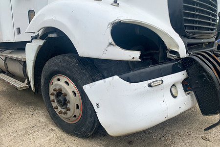 在汽车垃圾场发生交通事故后被遗弃的坠毁卡车的特写，一辆没有前灯的白色卡车的前保险杠腐烂。