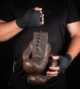 拳击黑摄影照片_穿黑衣服的运动员拿着非常旧的复古皮革棕色 bo