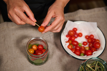 一位穿着黑色厨师围裙的家庭主妇在家庭厨房腌制成熟多汁的樱桃番茄的俯视图