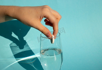 蓝色背景下，一只手将溶解的碳酸阿司匹林片剂放入一杯水中