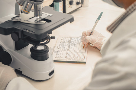 临床分析师写下在显微镜下检查的实验室样本的结果